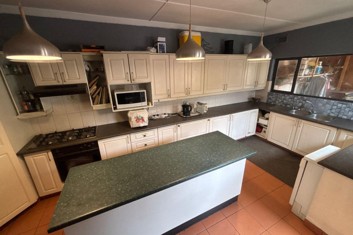 A functional kitchen featuring ample built-in cabinetry, a central island, gas hob, built-in oven, and tiled finishes throughout.