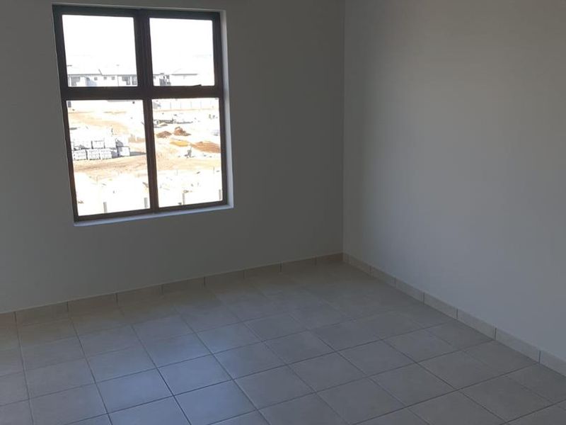A clean, empty bedroom featuring neutral tiled flooring, a large aluminium window, and a simple ceiling light fixture.