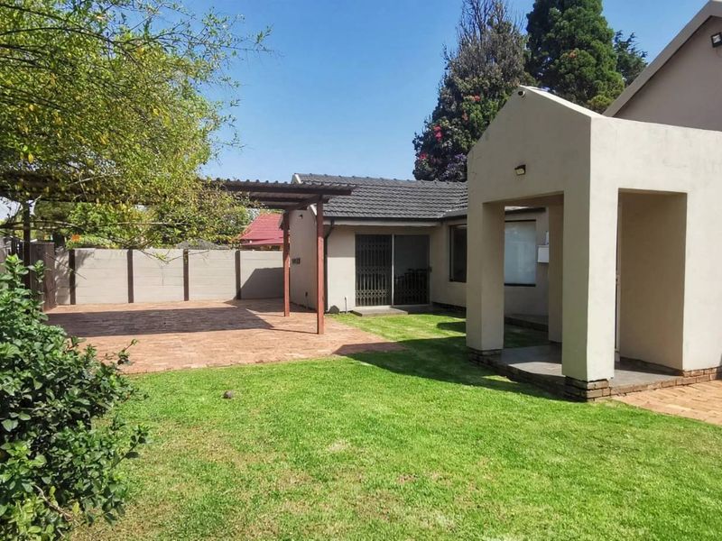 Rear view of the property featuring a paved patio area with a timber pergola, a well-maintained lawn, and secure boundary walls.