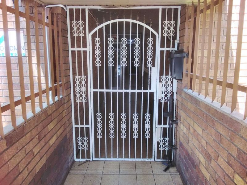 A secure apartment entrance featuring a white metal security gate, brick walls, and tiled flooring, providing a functional and protected entry point.