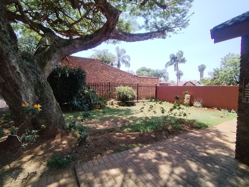 A private garden area featuring brick paving, established trees, and secure perimeter walling with metal fencing.