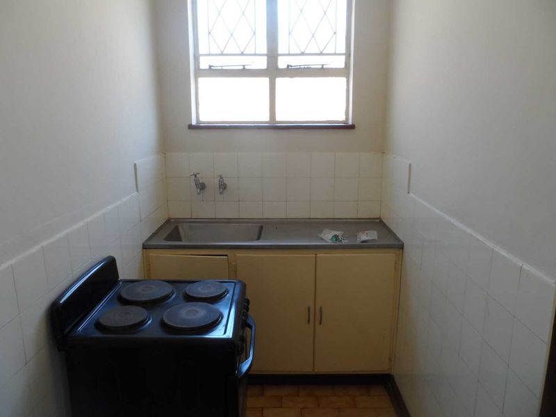 A compact, functional kitchen area featuring a stainless steel sink, tiled splashback, and an electric stove, offering potential for modernization.