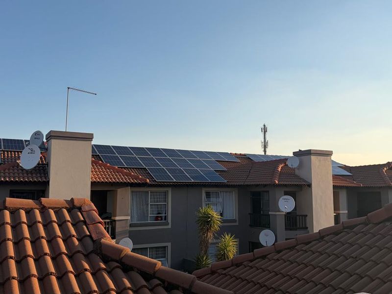 An elevated view of an apartment complex roof featuring installed solar panels, terracotta roof tiles, and multiple satellite dishes.
