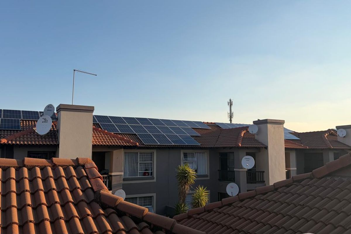 An elevated view of an apartment complex roof featuring installed solar panels, terracotta roof tiles, and multiple satellite dishes.