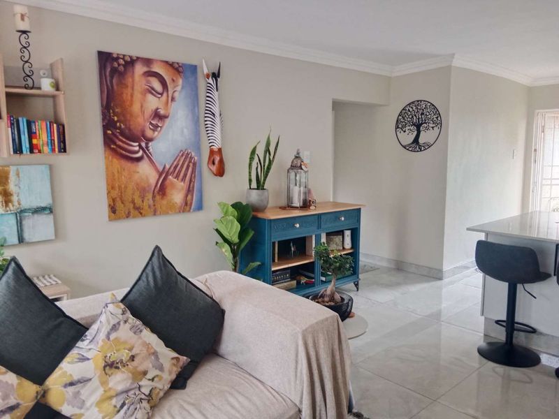 An open-plan living area featuring polished tiled flooring, a kitchen island, and neutral wall finishes with decorative ceiling cornicing.