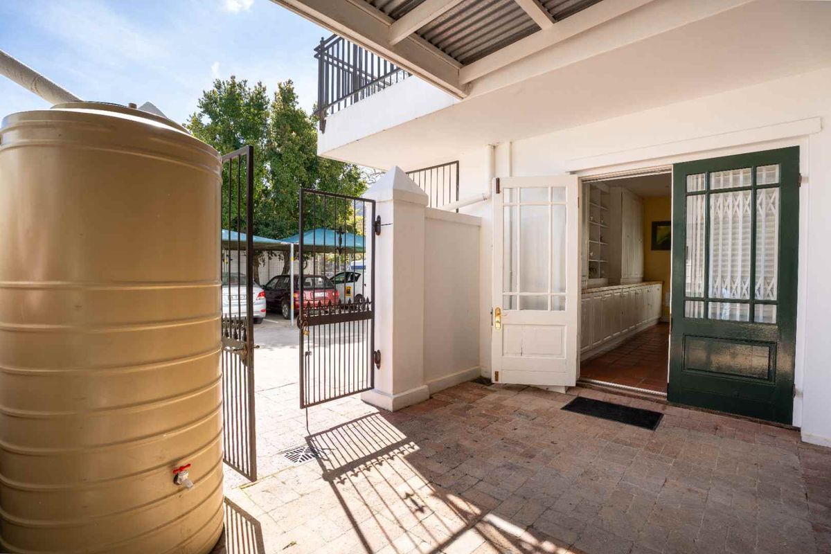 Rear exterior area featuring brick paving, a water storage tank, and access to the interior through a classic timber-framed glass door.