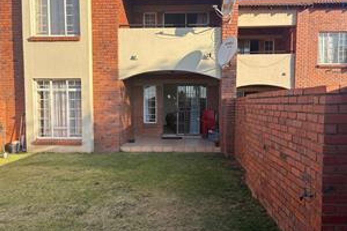Rear view of the apartment featuring a private garden, brick facade, and a covered patio area with sliding door access.