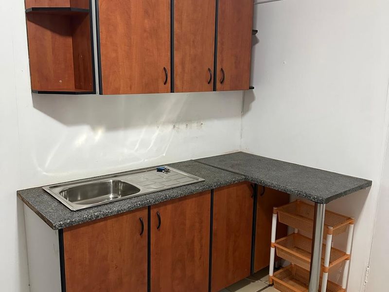 A compact kitchen area featuring wood-look laminate cabinetry, a stainless steel sink, and tiled flooring, offering a functional space ready for modernization.