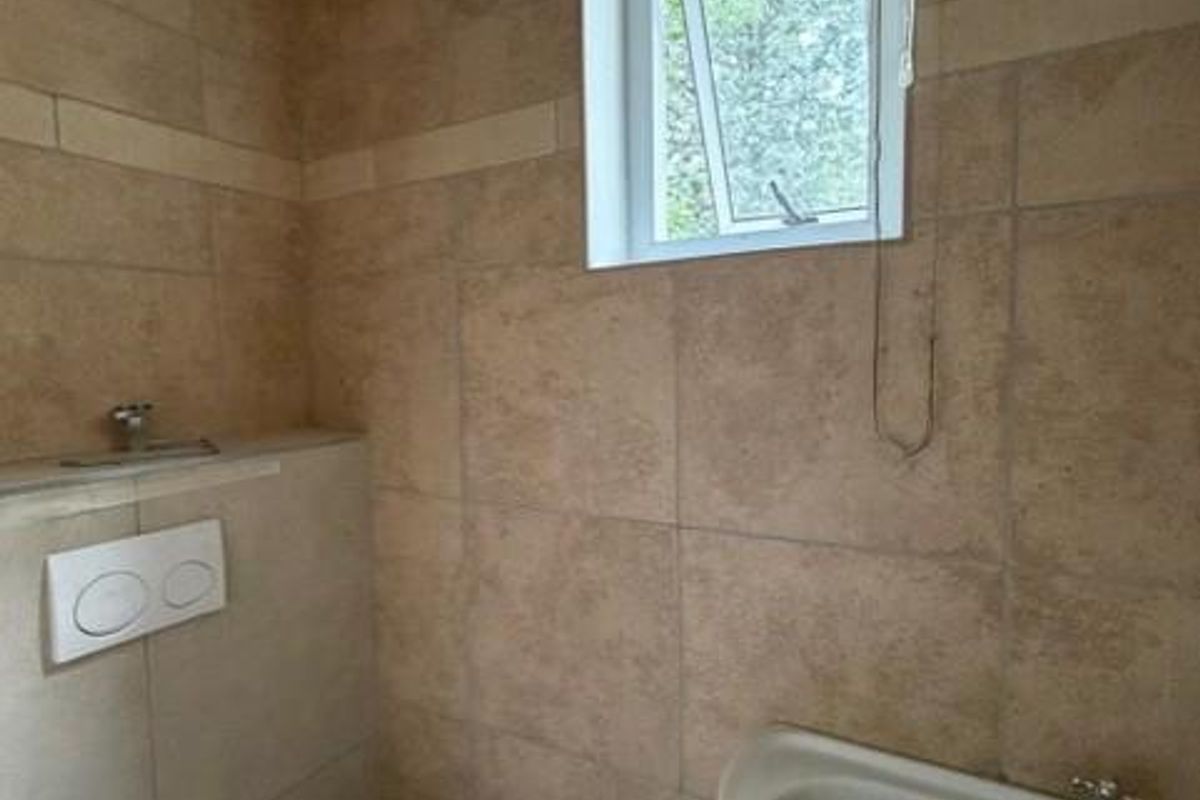 A compact office restroom featuring a pedestal sink, wall-mounted toilet, and neutral-toned wall tiling.