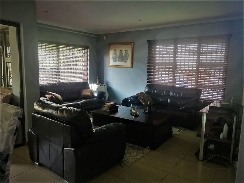 A spacious living room featuring tiled flooring, recessed downlighting, and large windows fitted with venetian blinds.