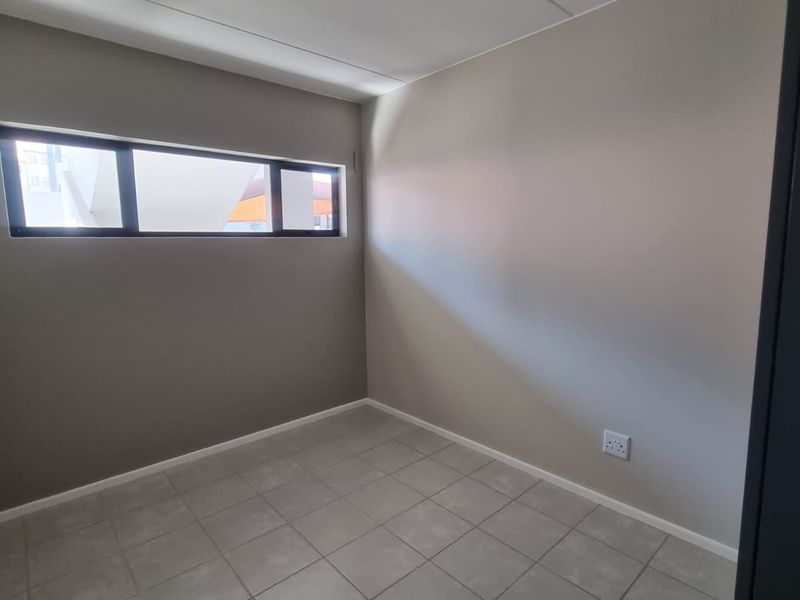 A clean, empty bedroom featuring neutral wall tones, tiled flooring, and a horizontal clerestory window providing natural light.