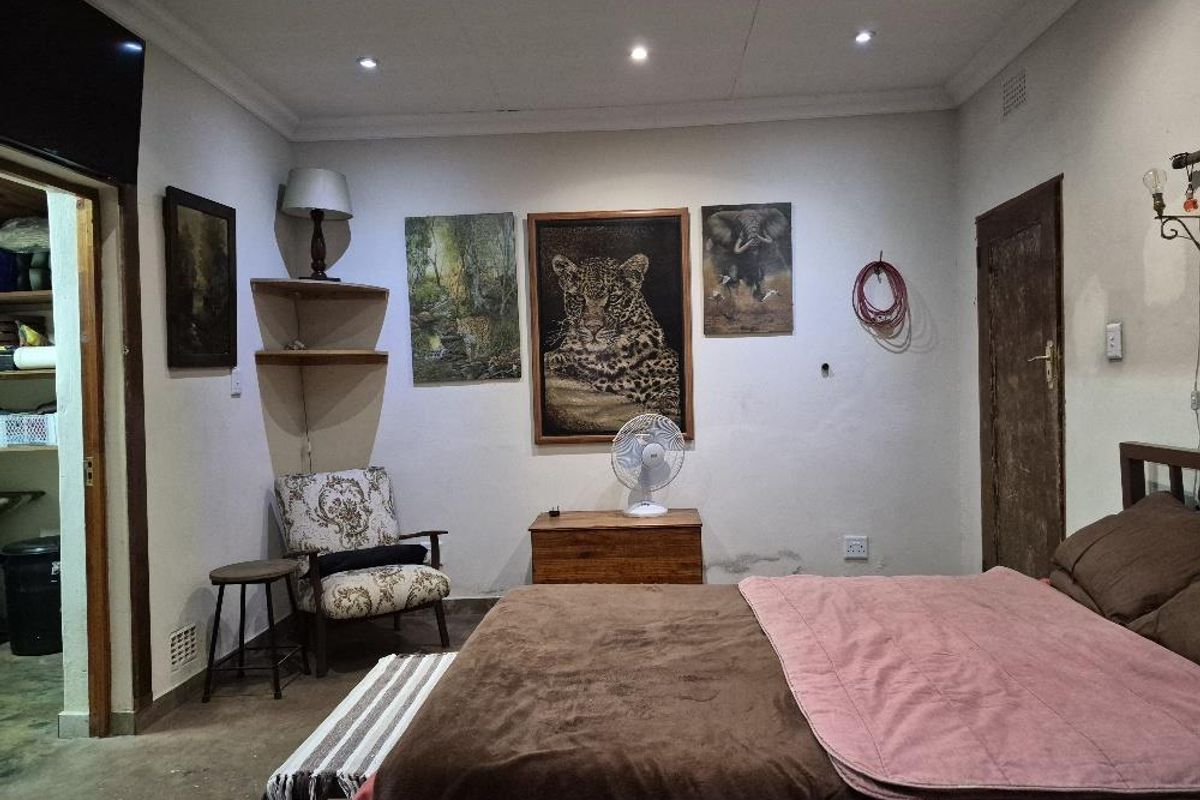 A bedroom featuring recessed downlighting, built-in corner shelving, and a solid wood door, showing signs of wear on the walls and door finish.