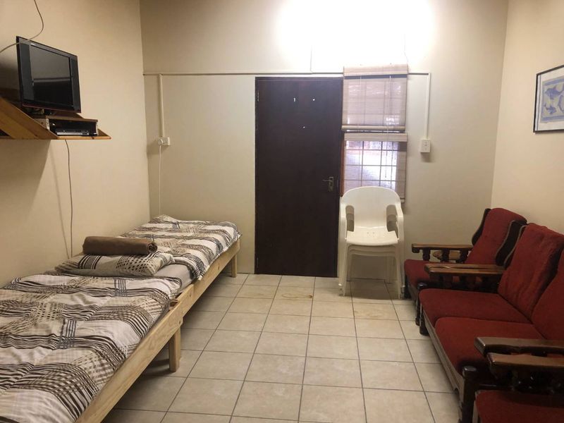 A basic bedroom featuring tiled flooring, a timber door, and a window with blinds. The space shows signs of wear and dated finishes.