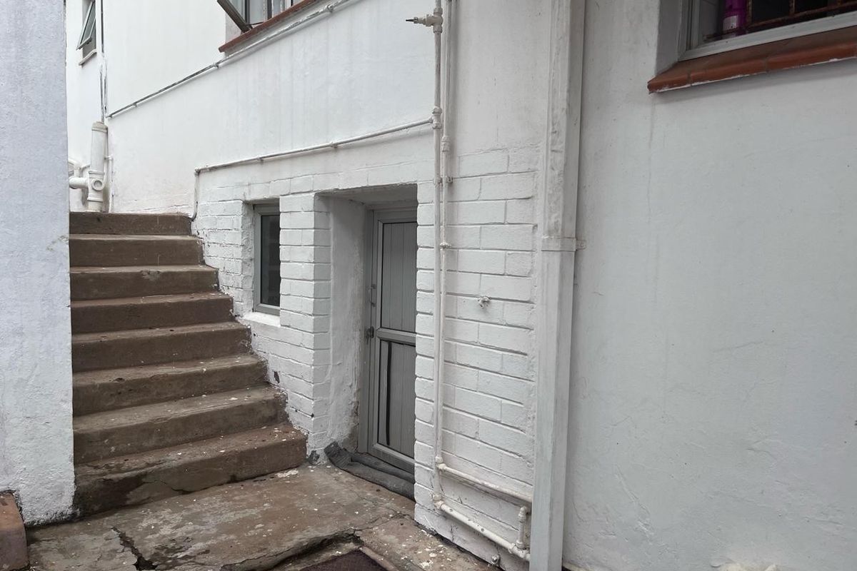 Exterior view of a rear building facade featuring painted brickwork, a concrete staircase, and an aluminium door with visible signs of wear.