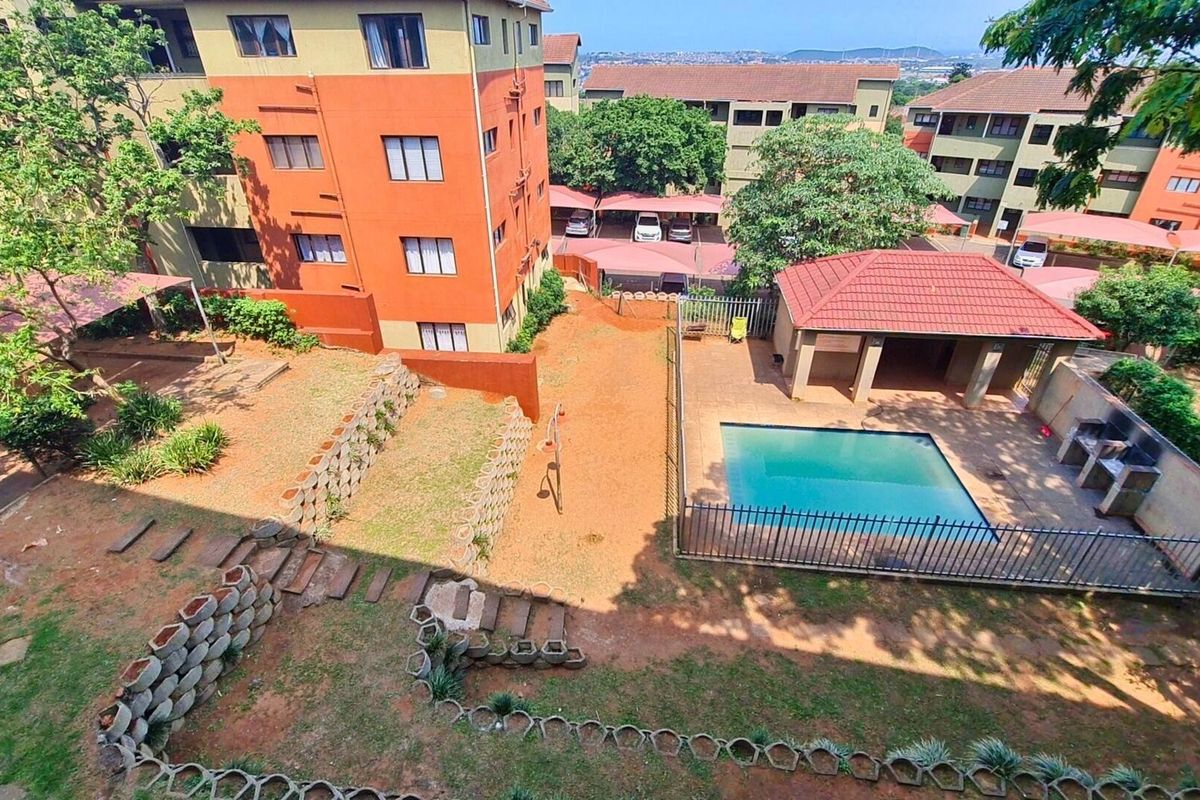 Aerial view of the apartment complex grounds featuring a communal swimming pool, lapa with built-in braai, carports, and landscaped garden areas.