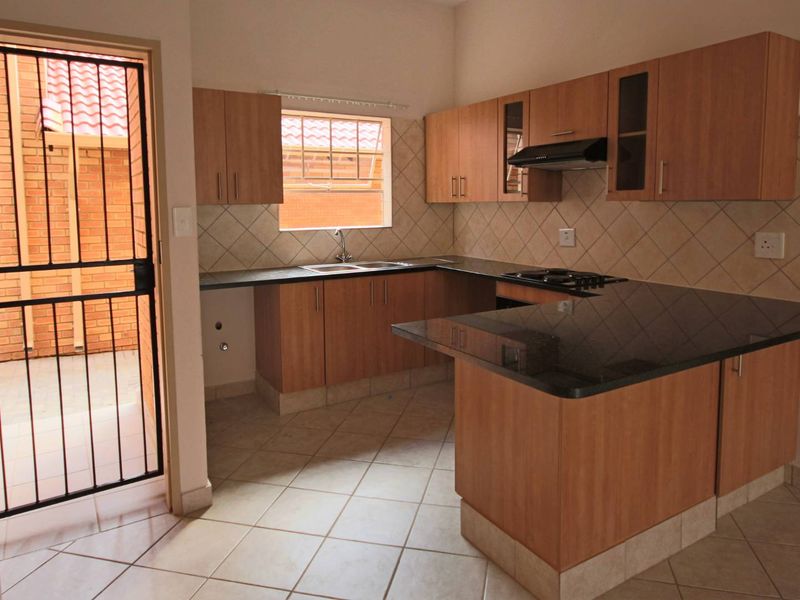 A functional kitchen featuring laminate cabinetry, granite countertops, a built-in hob with extractor fan, and direct access to an exterior courtyard.