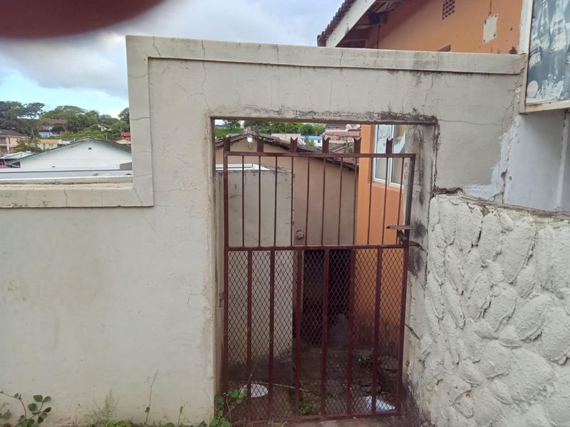 A rear exterior view showing a weathered masonry boundary wall with stone cladding and a rusted metal security gate leading to the property.