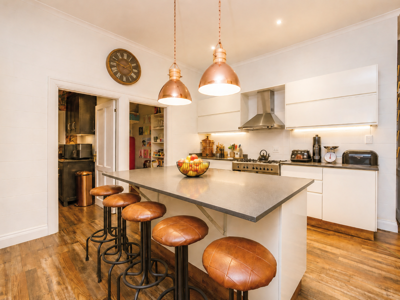 Modern kitchen featuring a central island with stone countertops, built-in gas cooktop, stainless steel extractor, and warm pendant lighting, complemented by hardwood flooring.