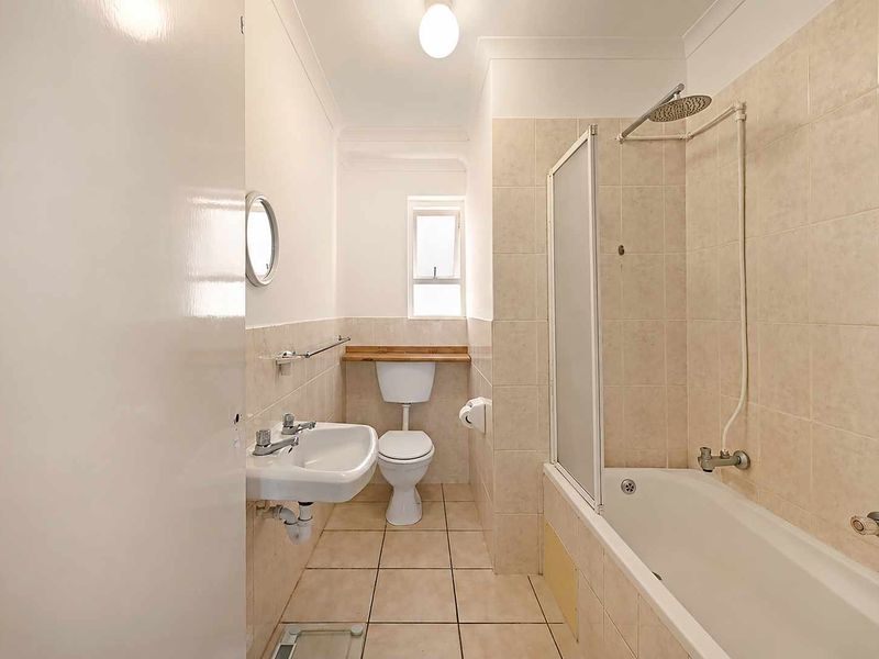 A functional bathroom featuring a bathtub with shower attachment, wall-mounted basin, and toilet, finished with neutral floor and wall tiling.