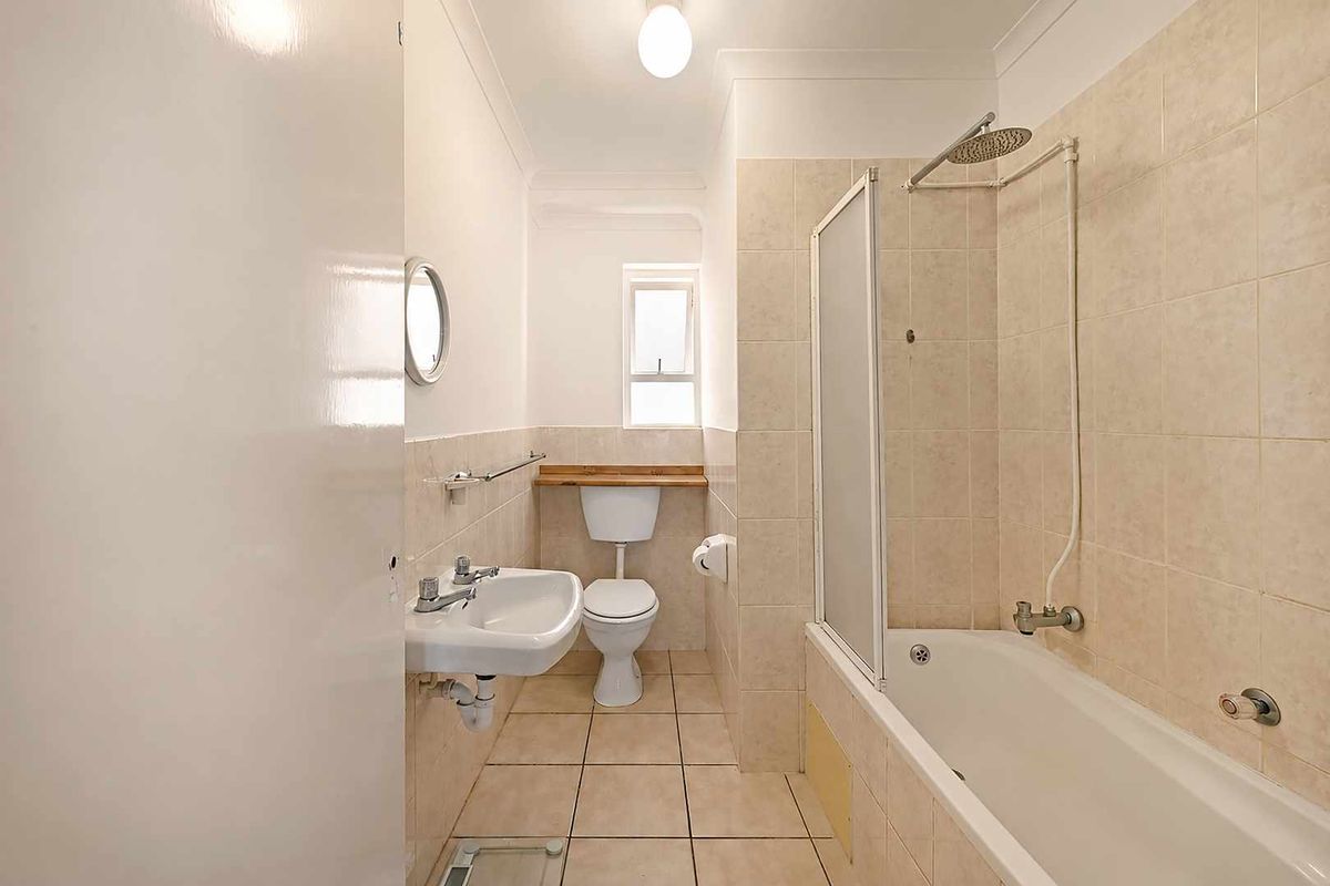A functional bathroom featuring a bathtub with shower attachment, wall-mounted basin, and toilet, finished with neutral floor and wall tiling.