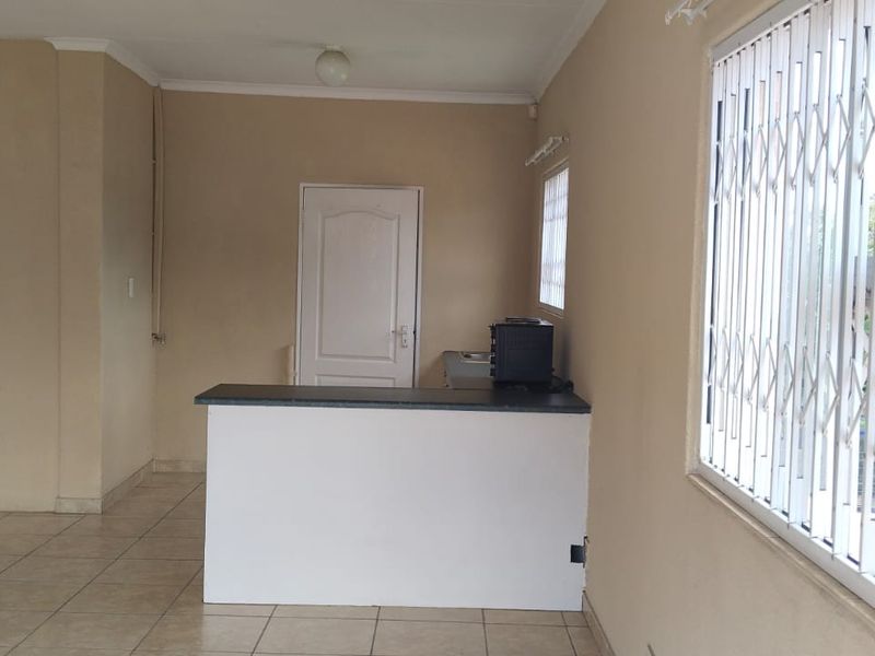 An open-plan living area featuring tiled flooring, a breakfast bar, and windows fitted with security gates.