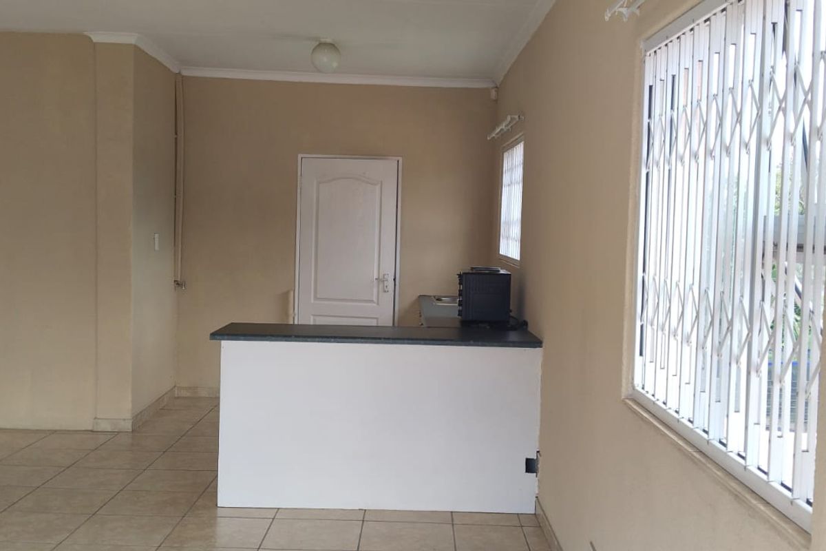 An open-plan living area featuring tiled flooring, a breakfast bar, and windows fitted with security gates.