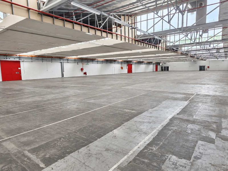 Expansive industrial warehouse space featuring high ceilings with exposed steel trusses, abundant natural light from skylights, and durable concrete flooring.