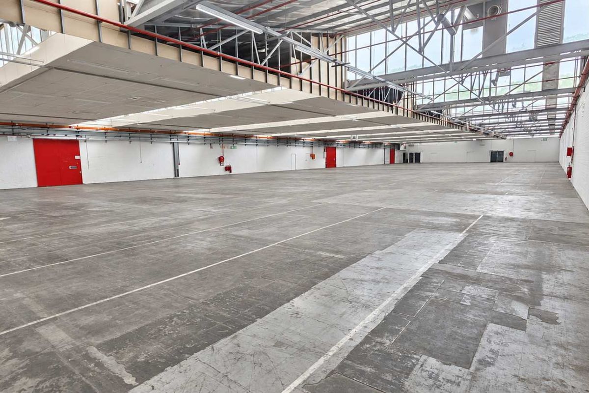 Expansive industrial warehouse space featuring high ceilings with exposed steel trusses, abundant natural light from skylights, and durable concrete flooring.