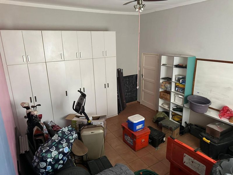 A bedroom featuring built-in cupboards, tiled flooring, and a ceiling fan, currently utilized as a storage space.