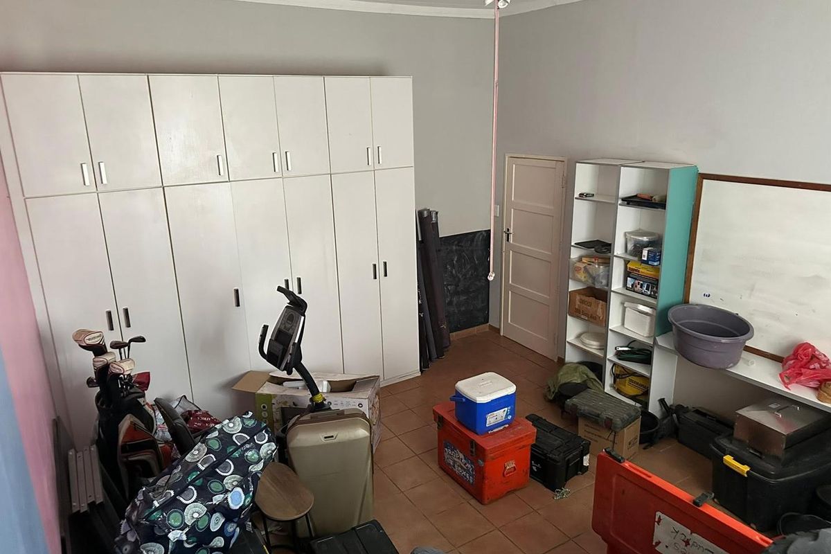 A bedroom featuring built-in cupboards, tiled flooring, and a ceiling fan, currently utilized as a storage space.