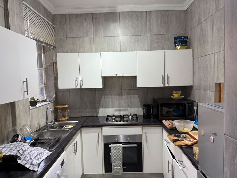 A functional kitchen featuring white cabinetry, dark granite countertops, a gas hob, built-in oven, and full-height grey wall tiling.