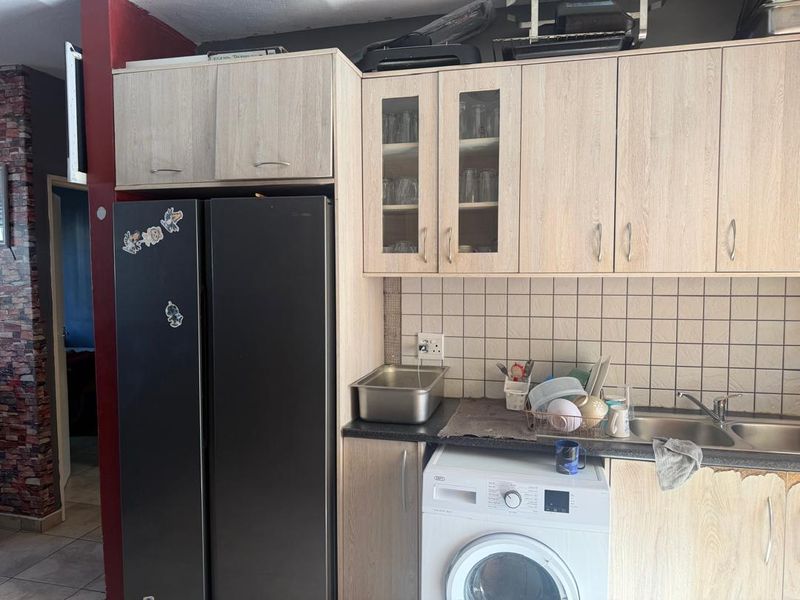 Compact kitchen area featuring light wood-look cabinetry, tiled backsplash, stainless steel sink, and integrated space for a washing machine.