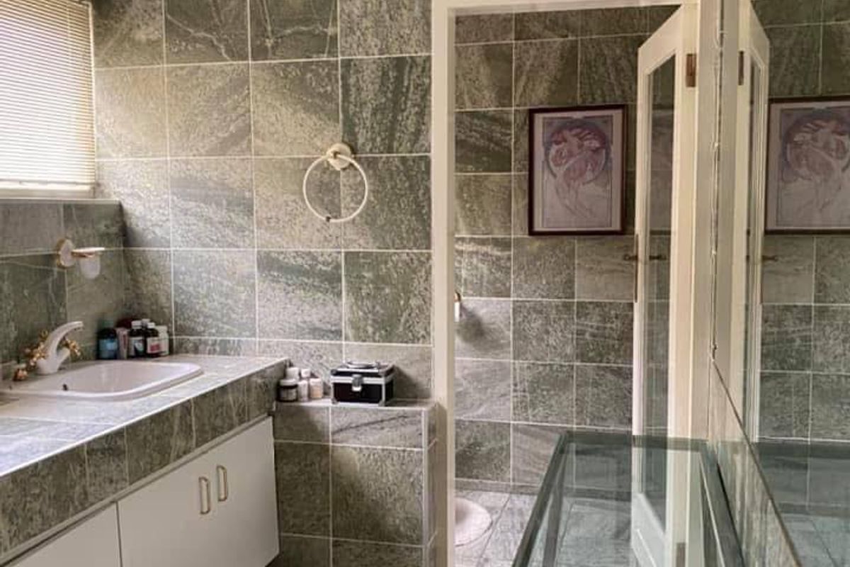 A bathroom featuring stone-tiled walls and vanity, white cabinetry, and a separate toilet area accessed through a glass-paneled door.