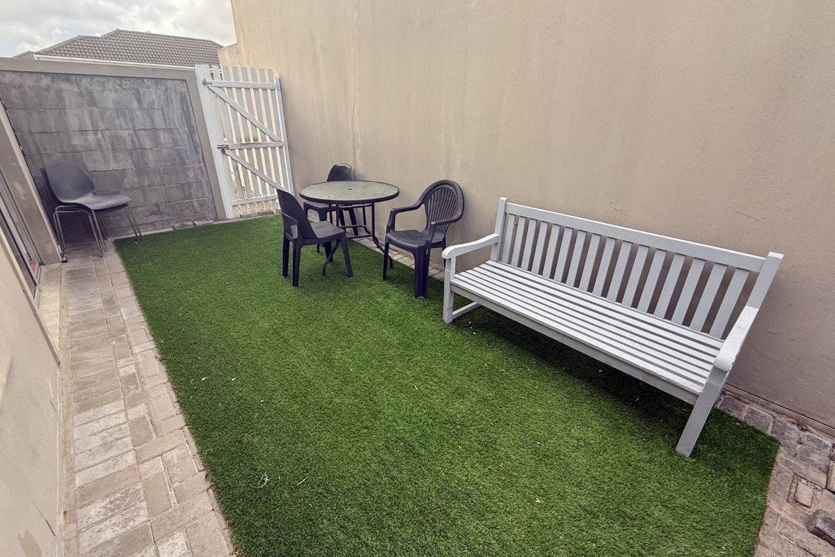 A compact, low-maintenance rear courtyard featuring artificial turf, paved borders, and a secure gated entrance.