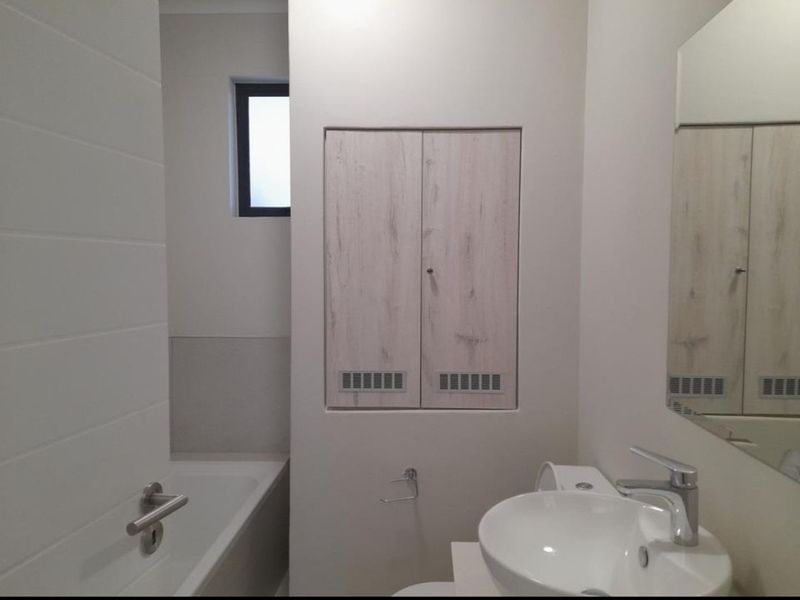 A clean, modern bathroom featuring a white bathtub, basin with mixer tap, and built-in storage cabinetry.