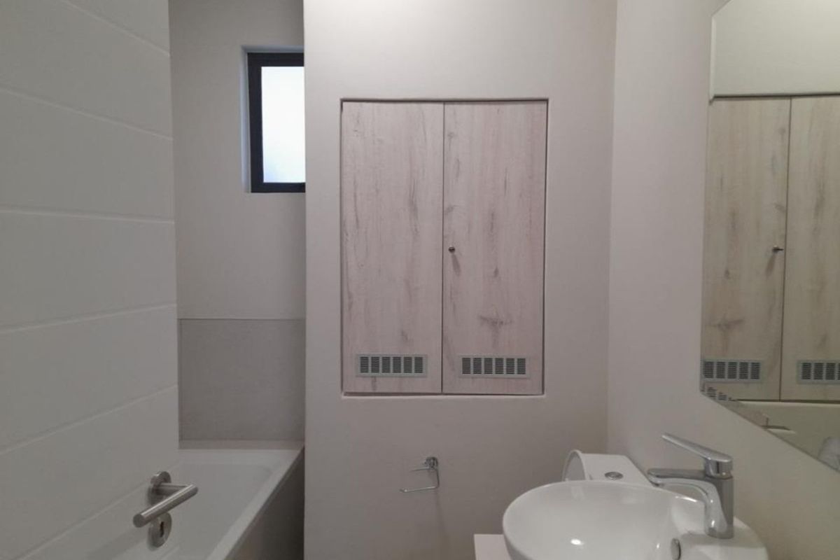 A clean, modern bathroom featuring a white bathtub, basin with mixer tap, and built-in storage cabinetry.
