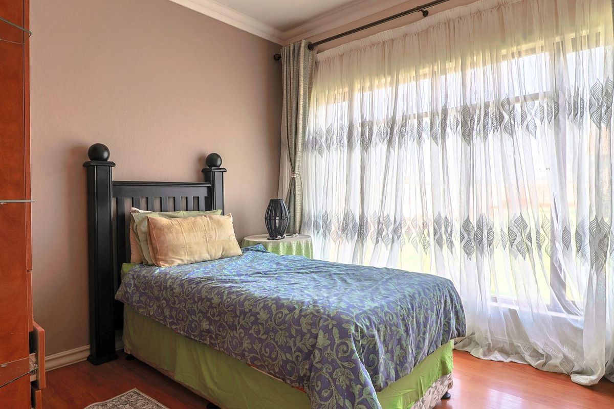 A well-lit bedroom featuring laminate flooring, neutral wall tones, and large windows dressed with floor-to-ceiling curtains.