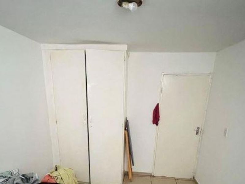 A simple bedroom featuring built-in wardrobe storage, tiled flooring, and a basic ceiling light fixture.