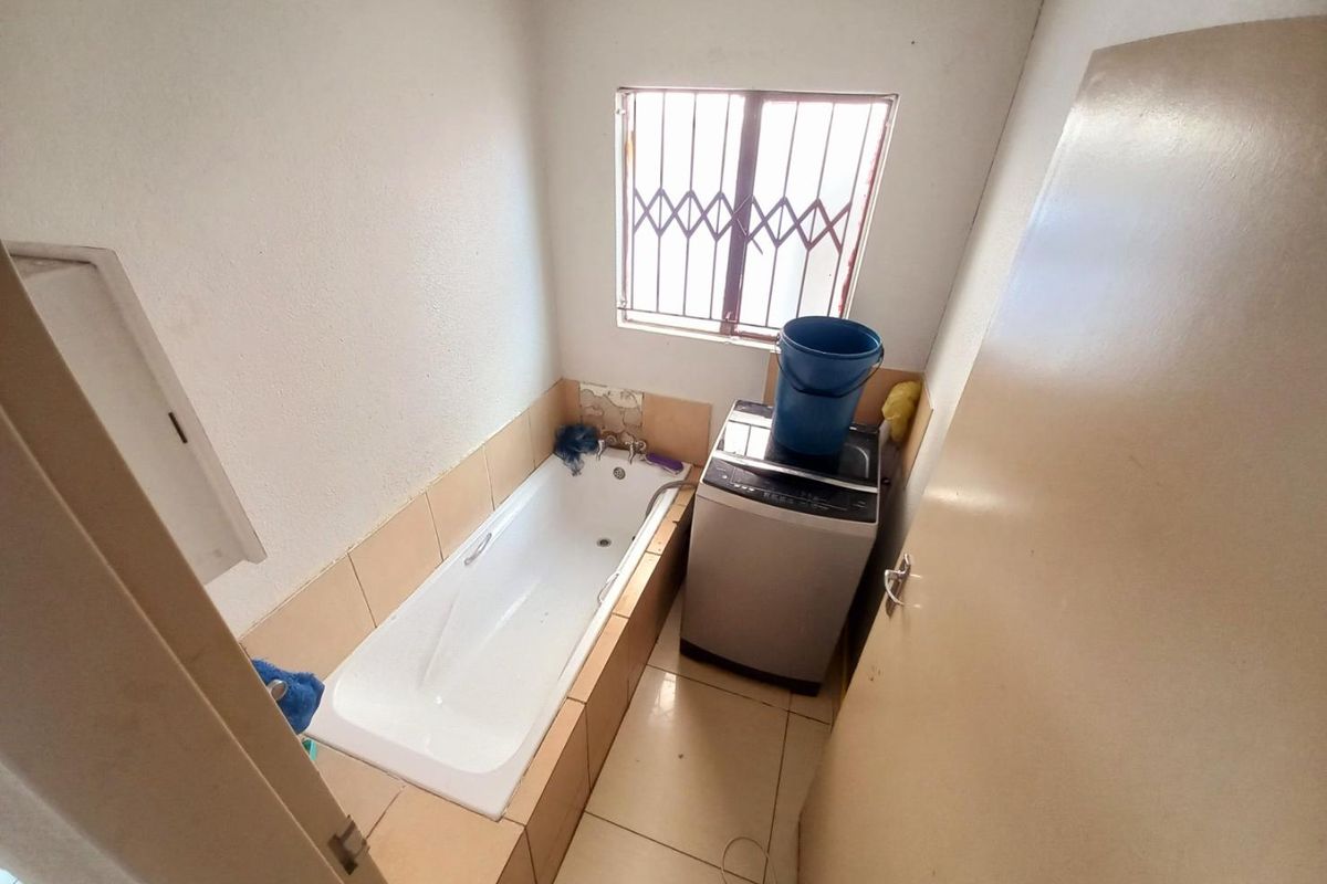 A compact bathroom featuring a built-in bathtub and dedicated space for laundry appliances, complete with a security-barred window.