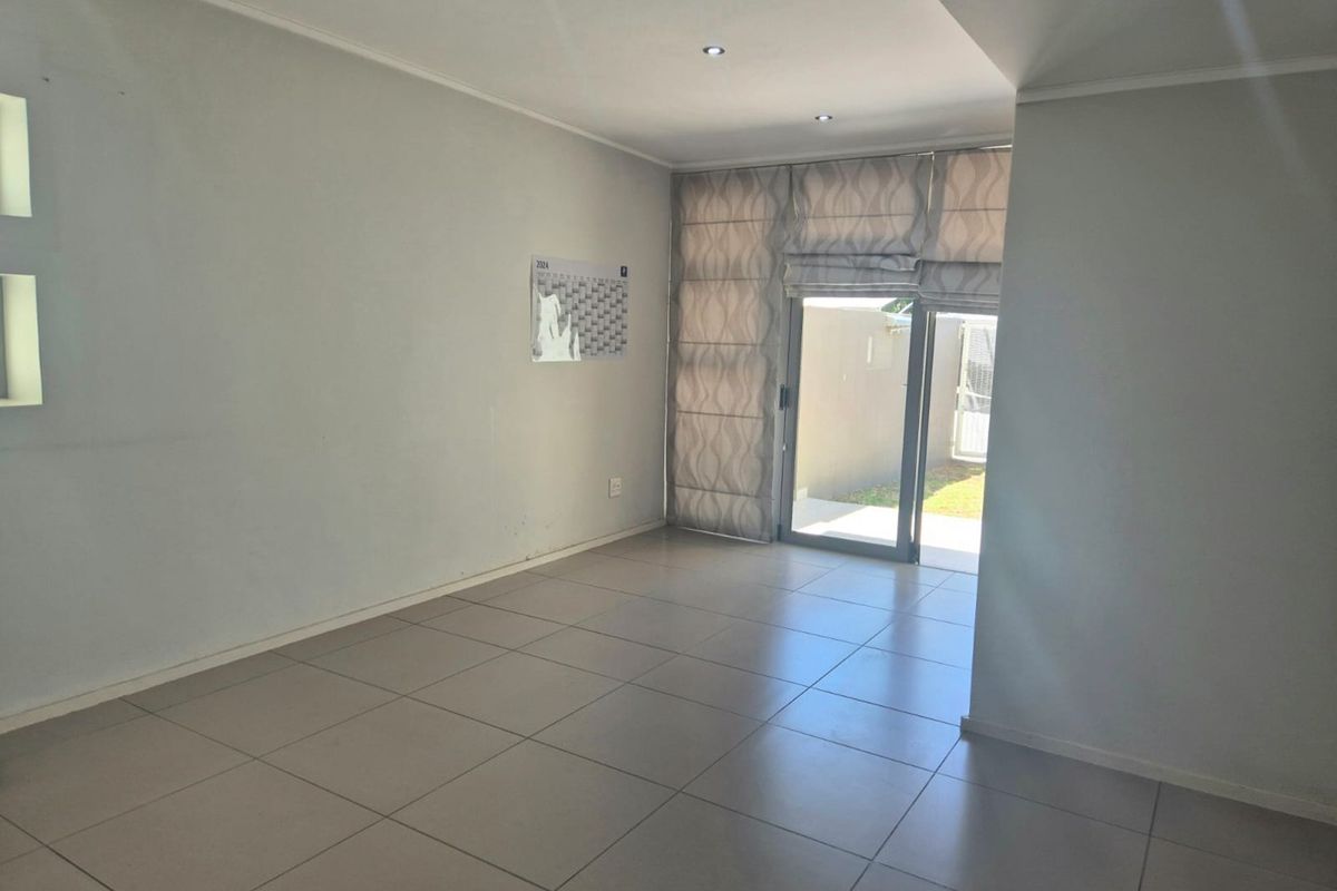 A bright, empty living area featuring neutral tiled flooring, recessed downlighting, and a sliding glass door providing access to the outdoor space.