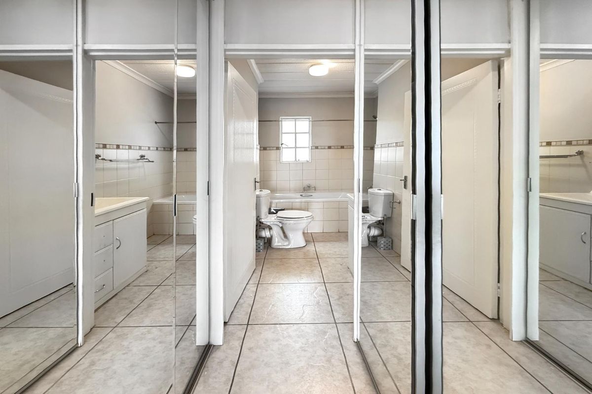 A functional bathroom featuring a built-in bathtub, toilet, and vanity unit, finished with neutral wall tiles and tiled flooring.