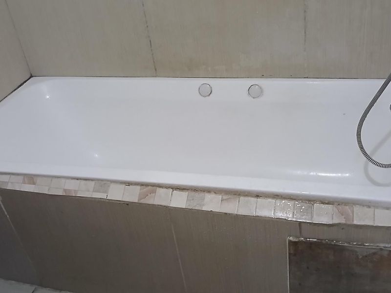 A bathroom featuring a built-in bathtub with a handheld shower attachment and tiled surround, requiring some maintenance and cosmetic updates.