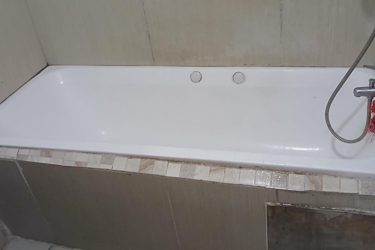 A bathroom featuring a built-in bathtub with a handheld shower attachment and tiled surround, requiring some maintenance and cosmetic updates.