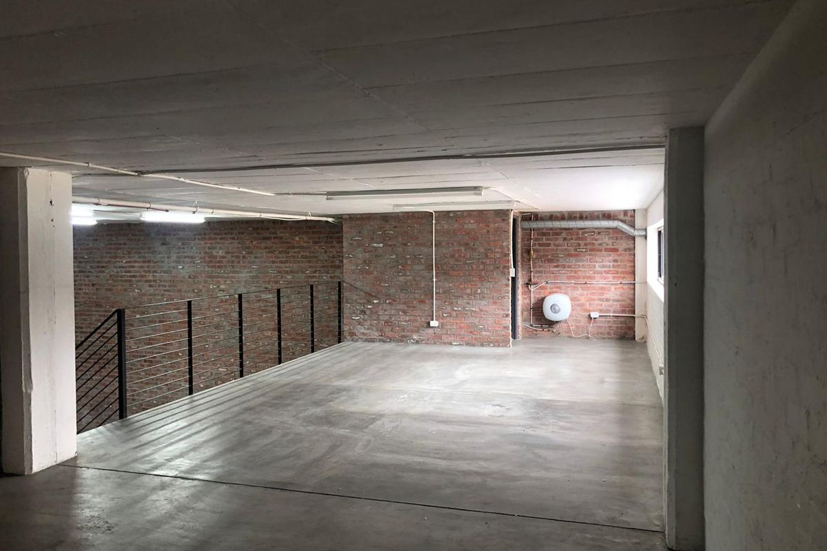 An expansive, industrial-style open plan space featuring exposed brick walls, polished concrete flooring, and a minimalist metal balustrade overlooking the lower level.
