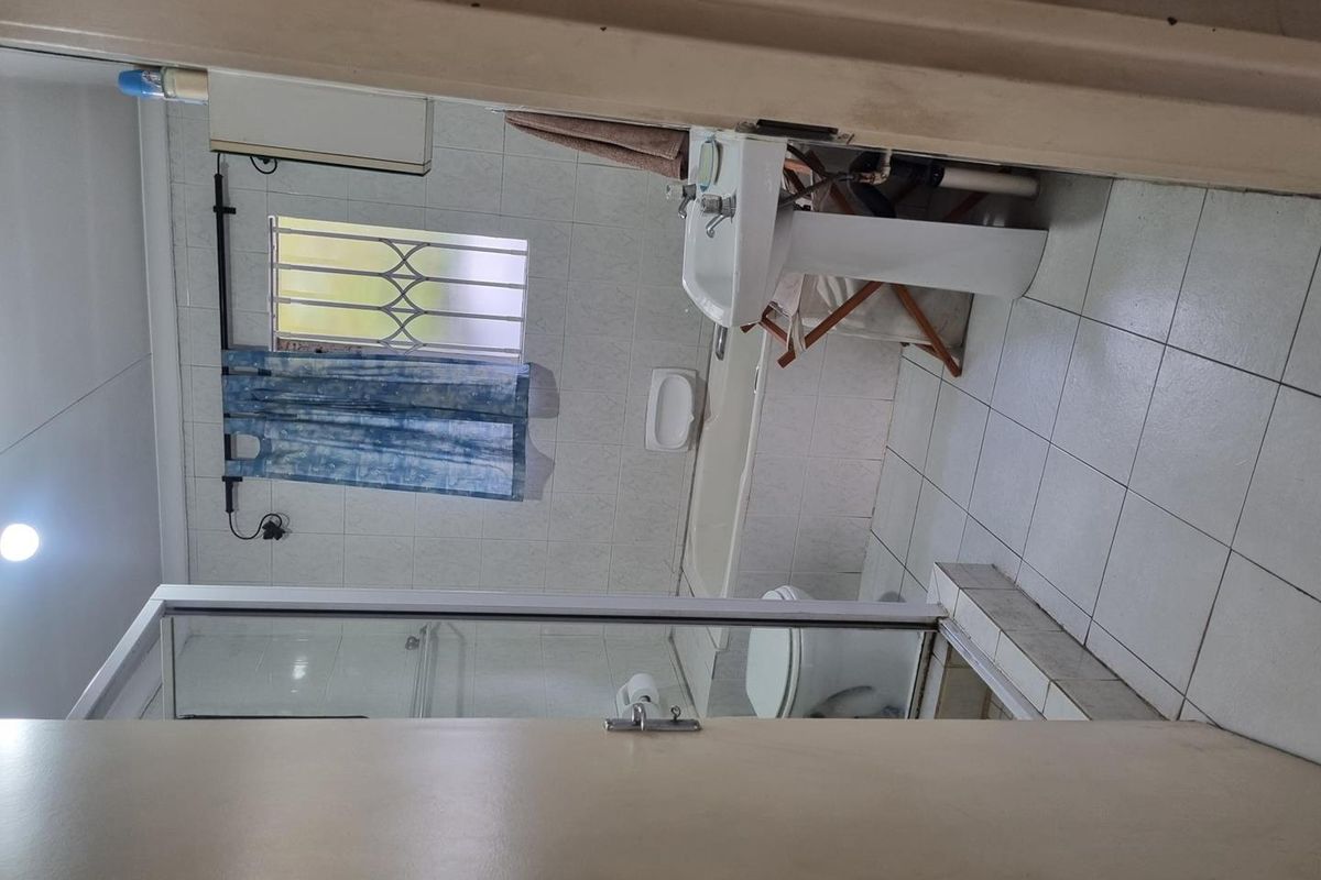 A functional bathroom featuring a pedestal basin, toilet, and a shower enclosure with tiled walls and flooring.