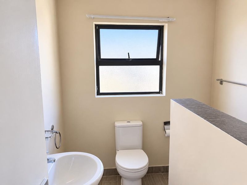 A clean and functional bathroom featuring a pedestal basin, toilet, and tiled flooring with a top-hung window for natural light.