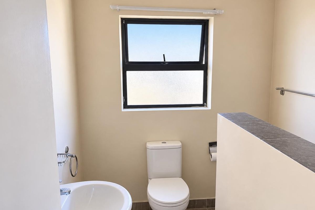 A clean and functional bathroom featuring a pedestal basin, toilet, and tiled flooring with a top-hung window for natural light.