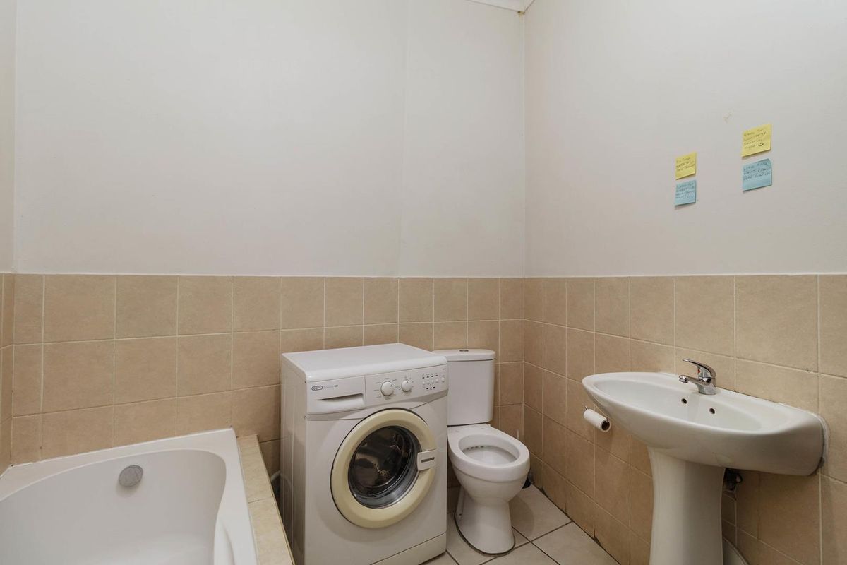 A functional bathroom featuring a bathtub, pedestal basin, and toilet, with tiled walls and floor.
