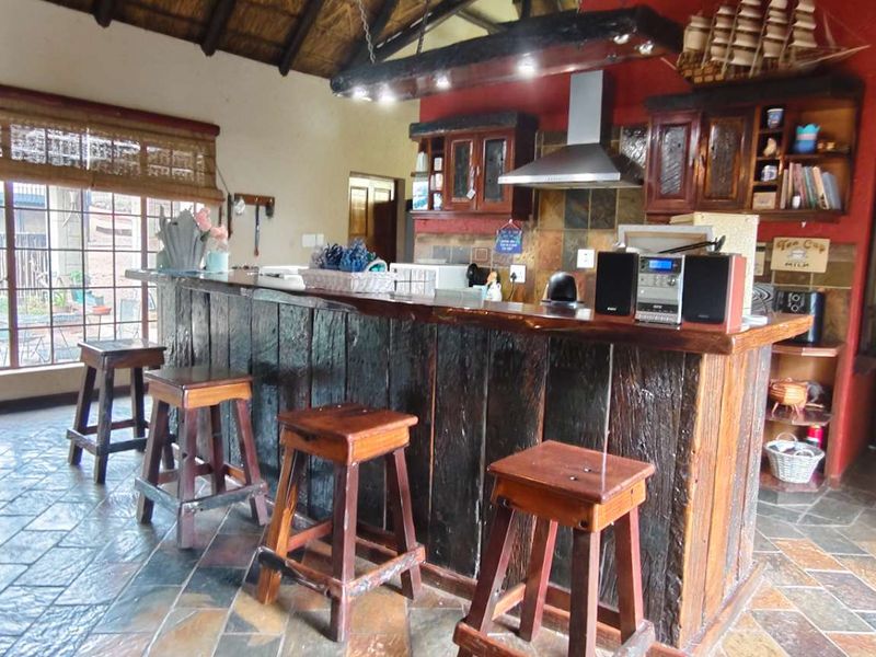 Rustic kitchen area featuring a large built-in timber bar counter, slate flooring, and exposed thatch ceiling with integrated extractor fan.