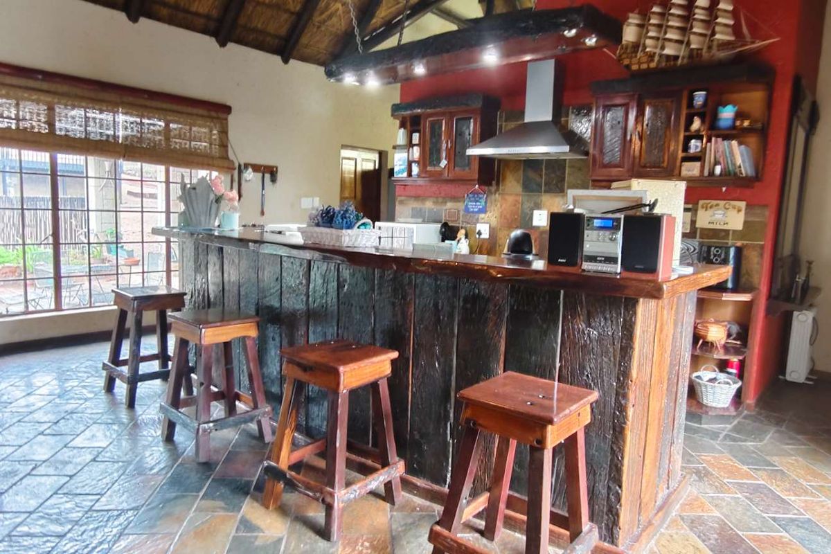 Rustic kitchen area featuring a large built-in timber bar counter, slate flooring, and exposed thatch ceiling with integrated extractor fan.